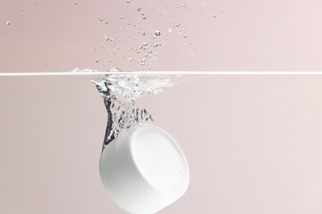 Beauty product tub falling into water with copy space background on pink background