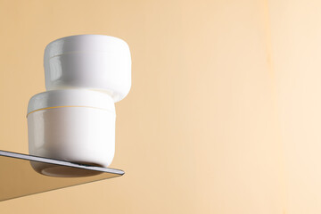 Beauty product white tubs on glass shelf, copy space on orange background