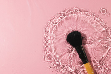 Beauty product make up brush in water with copy space background on pink background