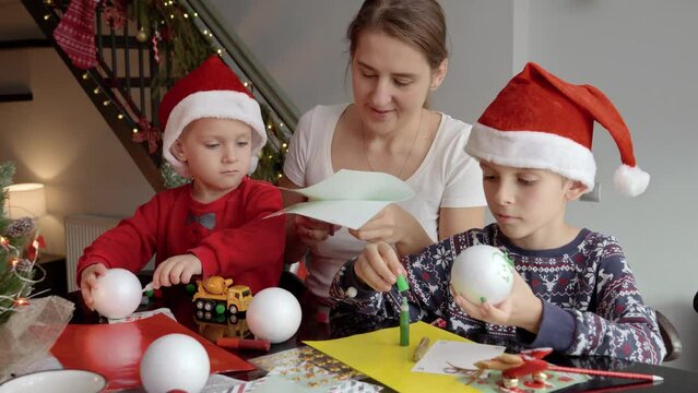 Happy family cutting out colorful paper and making baubles for celebrating Christmas and New Year. Winter holidays, family time together, kids with parents celebrating