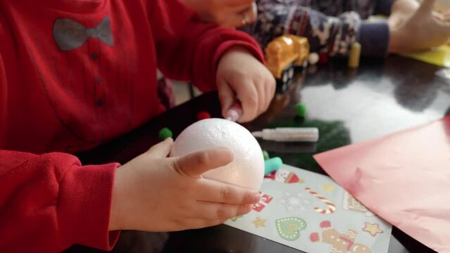Closeup of two boys making handmade Christmas baubles, painting and decorating them with glitter. Winter holidays, family time together, kids with parents celebrating