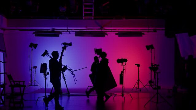 Professional filming pavilion with a neon cyclorama. The process of preparing for the shooting of a music video. Director, Cameraman and crew in Backstage.