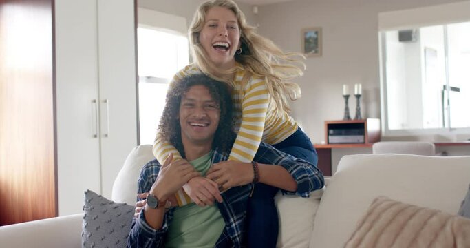 Portrait of happy diverse couple embracing and sitting on couch in living room, slow motion