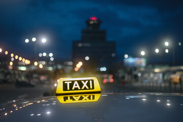 Selective focus on yellow taxi sign. Reflection in roof of car against airport terminal building at...
