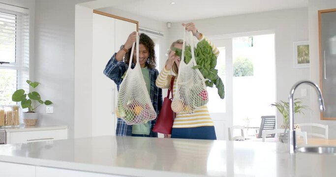 Happy diverse couple carrying and unpacking grocery shopping bags in kitchen, slow motion