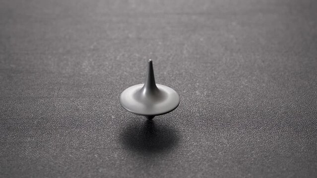Spinning top. The metal top rotates, slows down, sways and falls on dark background