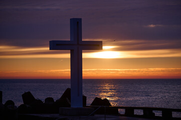 Christian Holy cross early in the morning at sunrise. The large cross stands on the edge of a breakwater on the sea coast