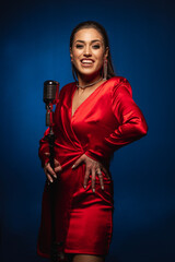 Fototapeta premium A pretty woman in a red dress sings on stage into a retro microphone