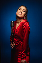 A pretty woman in a red dress sings on stage into a retro microphone