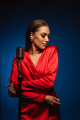 A pretty woman in a red dress sings on stage into a retro microphone