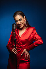 A pretty woman in a red dress sings on stage into a retro microphone