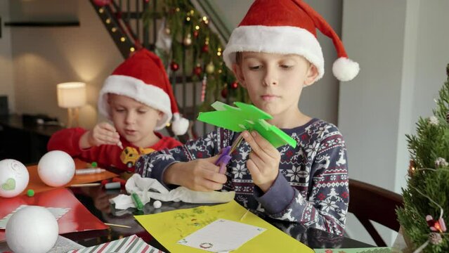 Two little boy preparing for Christmas cutting out paper decorations and garlands. Winter holidays, family time together, kids with parents celebrating