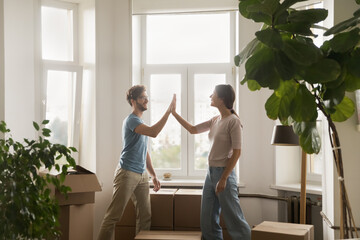 Young couple giving high five congratulate each other with relocation day finish carrying boxes with stuff enjoy move-in at own new house. Bank loan for young family, affordable dwelling, cohabitation - obrazy, fototapety, plakaty