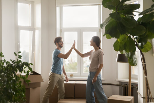 Young couple giving high five congratulate each other with relocation day finish carrying boxes with stuff enjoy move-in at own new house. Bank loan for young family, affordable dwelling, cohabitation