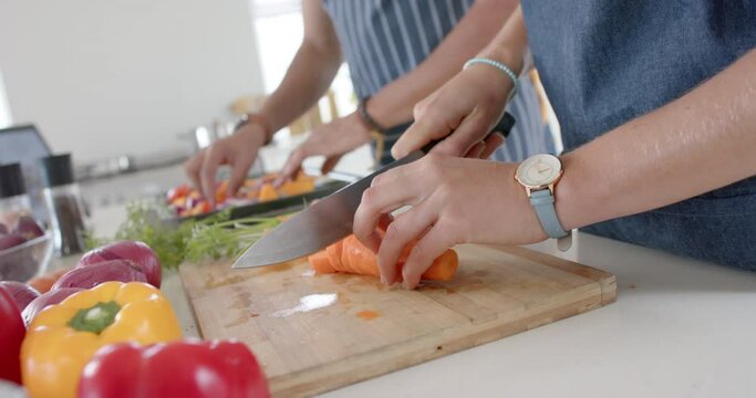 Happy diverse couple preparing fresh vegetables and wearing aprons in kitchen, slow motion