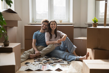 Portrait of happy young homeowner family sit on floor with boxes and decoration tiles samples,...