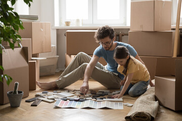 Young father and little daughter sit on floor choosing samples for house decoration, review...