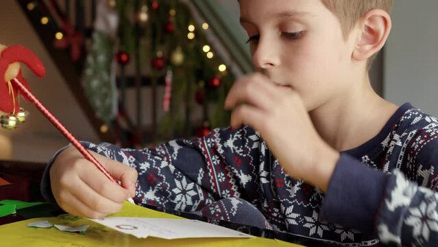 Closeup of little boy thinking of his wishes while writing a letter to Santa on Christmas.