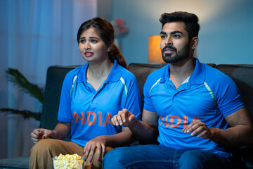 shocked Young couples while watching live cricket match on tv or television at home - concept of...