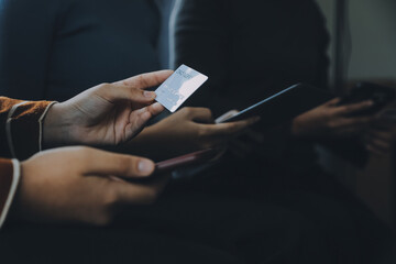 A credit card in the hands of a young businesswoman pays for a business on a mobile phone and on a desk with a laptop.