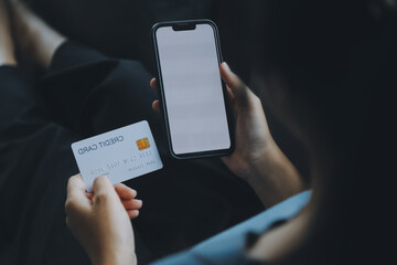 A credit card in the hands of a young businesswoman pays for a business on a mobile phone and on a desk with a laptop.