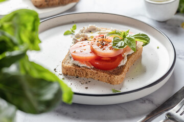Sandwich or toast with tomatoes, cream cheese, olive oil and basil on a plate on white marble background. Traditional italian mediterranean food