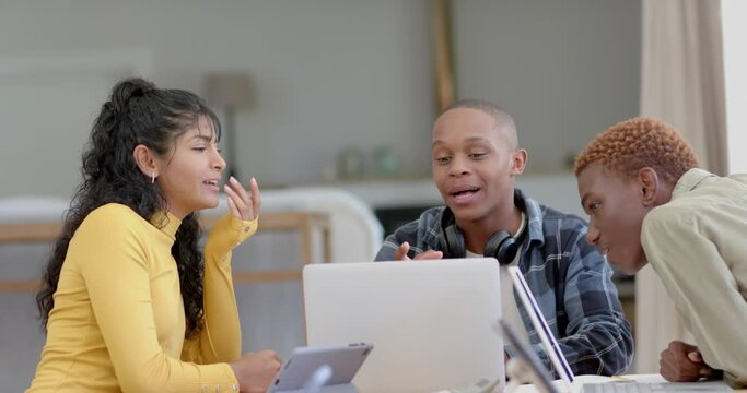 Happy diverse group of teenage friends studying at table with laptop at home, slow motion