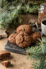 Homemade christmas chocolate cookies on wooden board and coffee on brown festive background with fir tree branches. Christmas holiday desserts