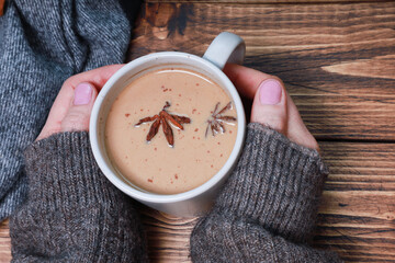 Female hands in woolen knitted sweater sleeves holding coffee mug, warming spicy latte. Cup of...