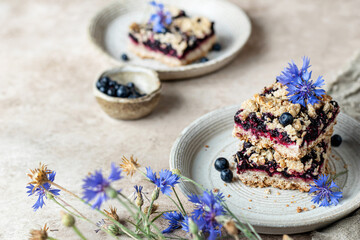 Baked oatmeal squares with fresh blueberry on beige background with cornflowers close up, text space. Menu, recipe
