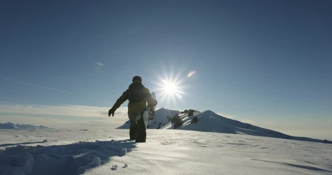 Silhouette of freeride snowboarder walking through deep snow in the mountains with snowboard towards the sun. Extreme off-trail freeriding, outdoor winter activities and adventure