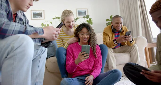 Happy diverse group of teenage friends using smartphones and laughing at home, slow motion