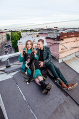 Fototapeta premium Beautiful couple in love with black dog on the roof at sunset in summer