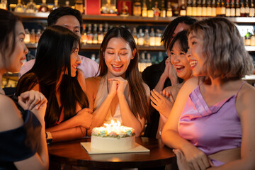 Beautiful Asian Woman is Savoring Her Birthday Festivities at a Restaurant or Bar, Surrounded by Friends Who Have Gathered to Joyfully Celebrate with Her.