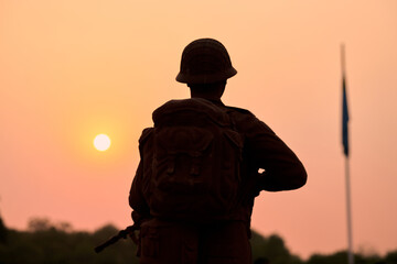 Rear view of silhouette of soldier in military gear holds weapon against bloody sunset - obrazy, fototapety, plakaty