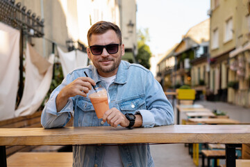 Urban man in sunglasses drinks healthy smoothie on street in city.