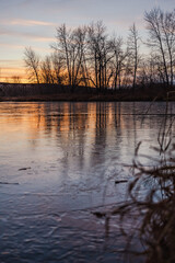 Frozen pond at sunset with trees in background