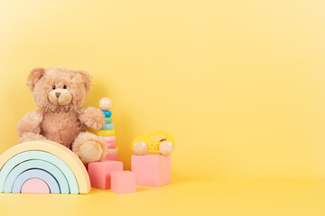 Educational kids toys collection. Teddy bear, wooden rainbow pink cubes and colorful balls on yellow background. Front view - obrazy, fototapety, plakaty