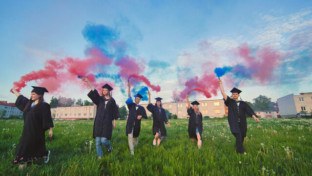 Students graduate with colored smoke walking through the meadow in the evening.
