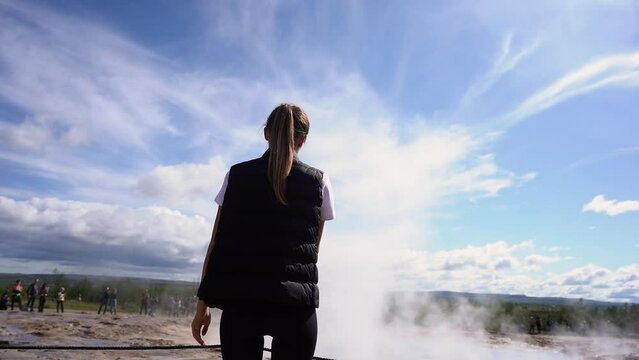 The tourist girl looks at the geyser in Iceland