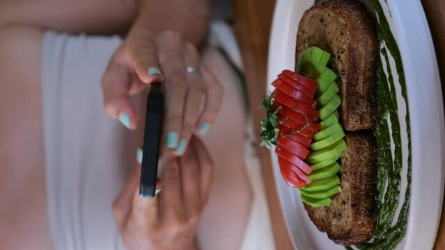 Vertical video food blogger takes photo of beautiful avocado toast with tomatoes, close-up. Cinematic video of avocado toast made from toasted rye bread, sliced avocado, tomatoes. Make photo of toast.