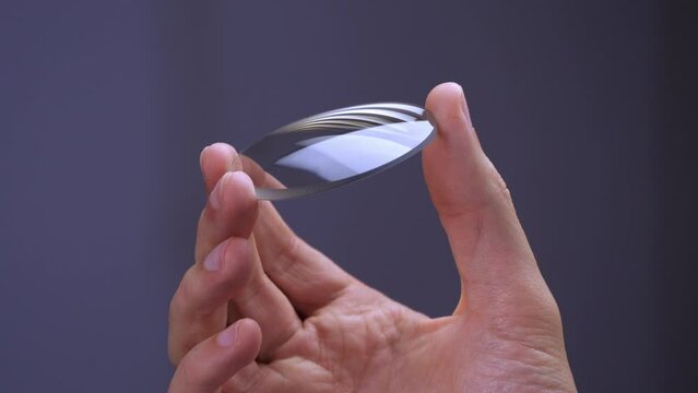Hand holds a circular glass lens for eyeglasses, modern technology for eyewear quality manufacturing video