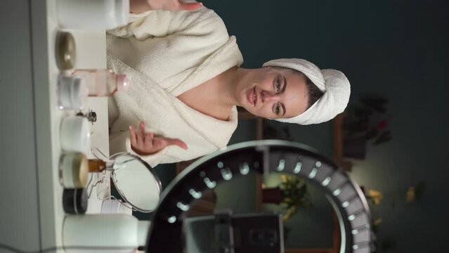 Beauty blogger filming daily skin care routine tutorial at camera on smartphone camera. Female Influencer live-streaming cosmetics product review in home. Vlogger cosmetic product.