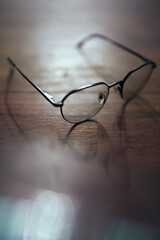 Photo of glasses on wooden table with bokeh and  blurred reflection. Shallow depth of field. Bad eyesight concept image with copy space.