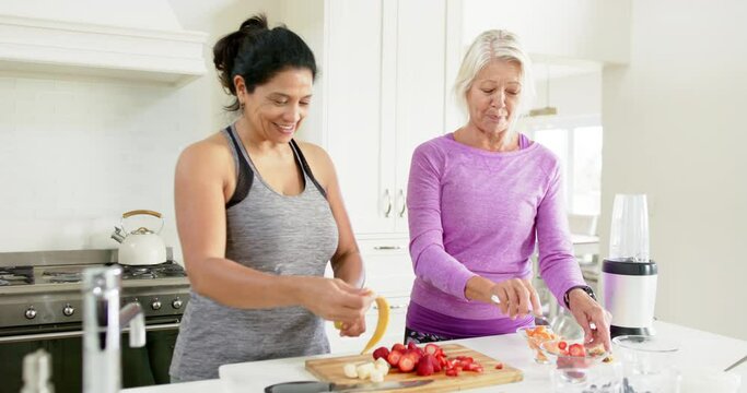 Two happy diverse senior women preparing fruits and laughing in sunny kitchen, slow motion