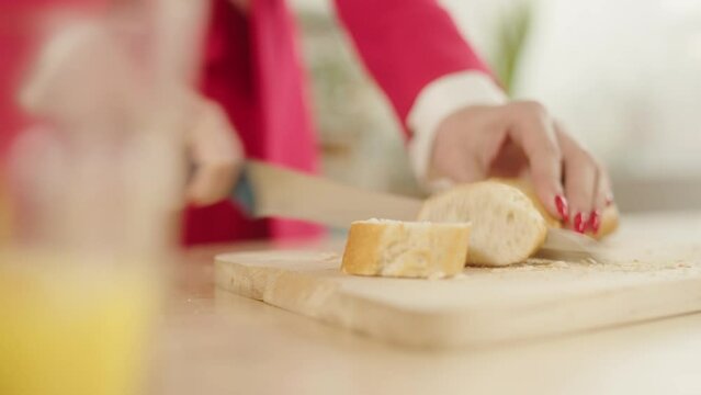 Woman in the red clothes Slicing A Loaf Of White Bread. Female hands cutting Sandwich on Wooden Board, close-up.
