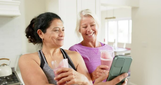 Two happy diverse senior women with cocktails doing selfie in kitchen, slow motion