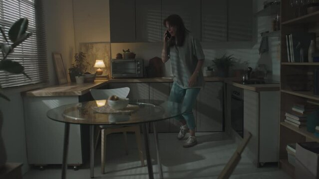 Long shot of scared woman talking on mobile phone with her mother after quarrel with abusive husband indoors