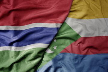 big waving national colorful flag of comoros and national flag of gambia .