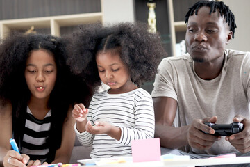 Happy family love bonding, African dad and daughter girl with curly hair enjoy spend time together at home, little child kid eating snack, father playing video game and her sister doing homework. - obrazy, fototapety, plakaty